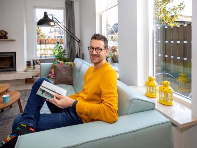 Sander Holterman leest een boek in zijn woonkamer